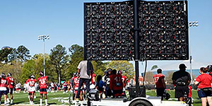 An 8K Solutions Lyvve Coach instant replay board is seen from behind, with the board facing a college football practice and coaches using it to show replays.