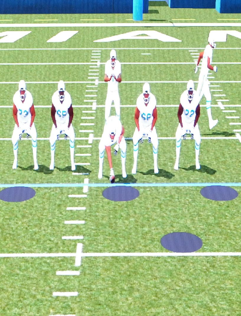 Animated football players appear on a 10 foot tall video wall as generated by 3D Playbook. The program developed by 8K Solutions uses available player tracking data to generate American football plays to help teams practice pre-snap alignment and assignment.