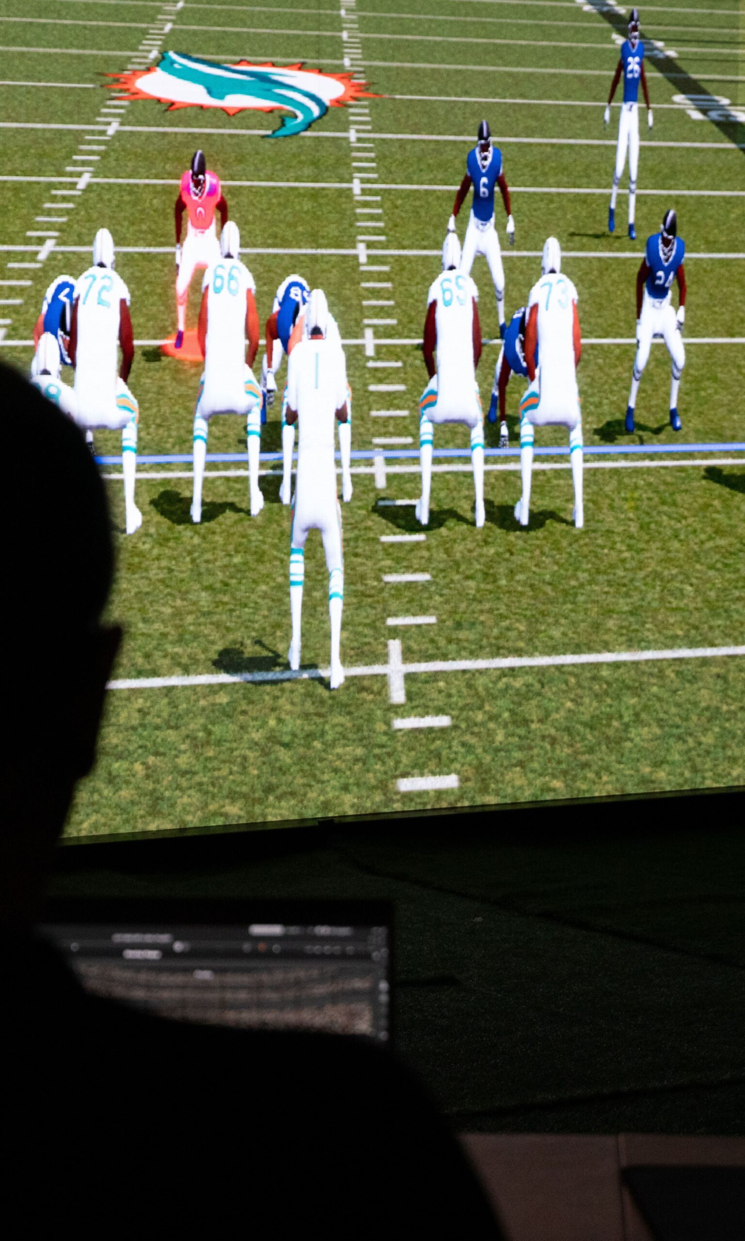 A coach sits at a computer creating plays on 3D Playbook that are projected onto a lifesize screen.