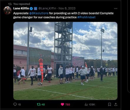 Screen capture of a tweet from Ole Miss football coach Lane Kiffin showing players at practice gathered around two large LED screens replaying video of the last play at practice. The tweet thanks 8K Solutions for making the screens, known as Lyvve Coach, available to his team as it conveys a pro mindset.