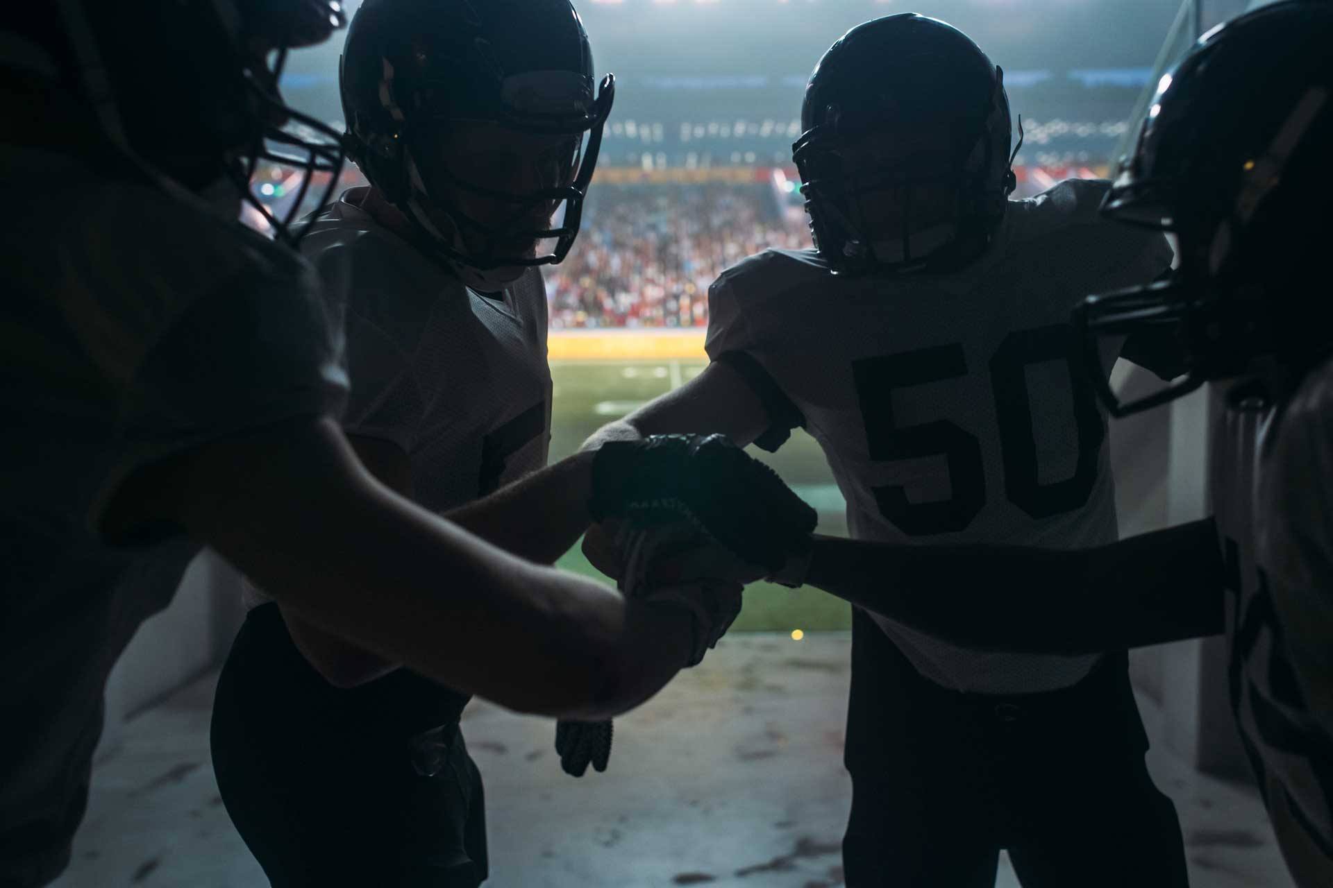 American football teammates backlit in a tunnel entrance to a football stadium gather to prepare before entering the game.